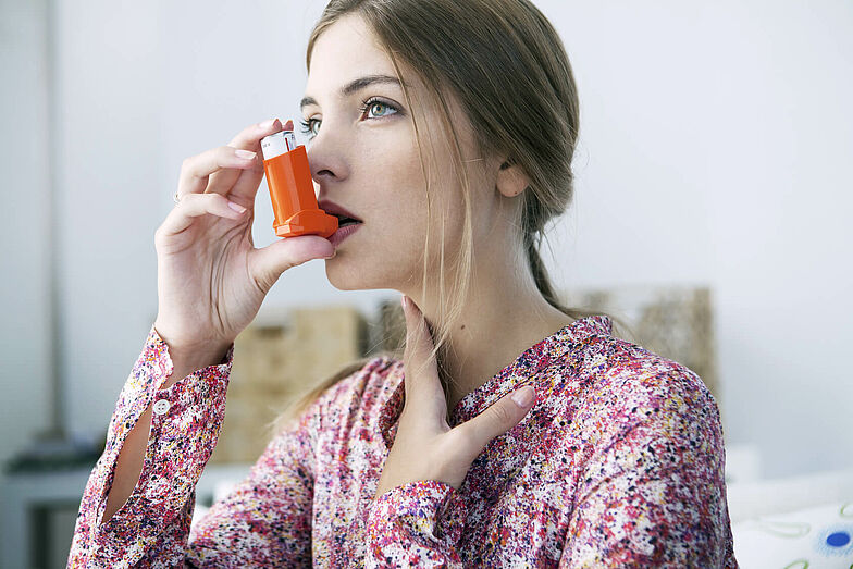 Eine junge Frau inhaliert mit einem Asthmaspray.